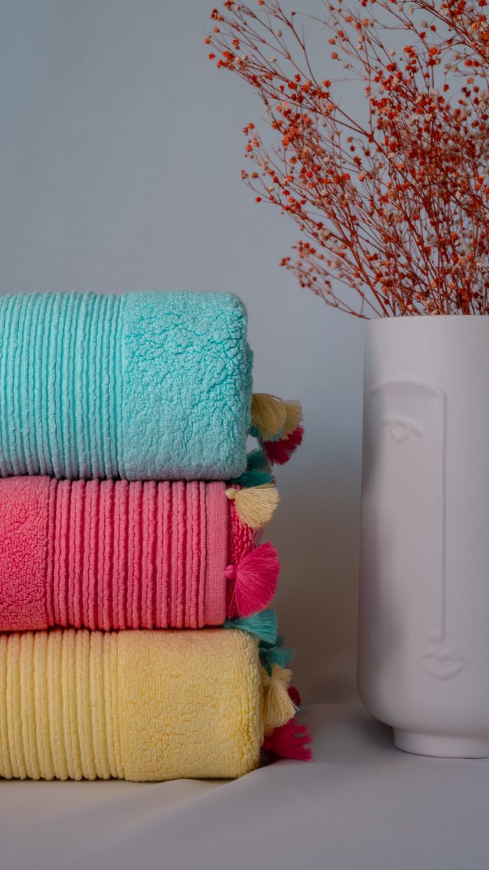 Stack of colorful towels with a decorative vase and dried flowers in a minimalist setting.