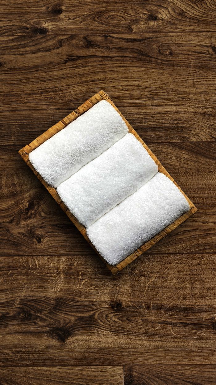 Three neatly rolled white towels on a bamboo tray placed on a wooden surface, perfect for spa themes.