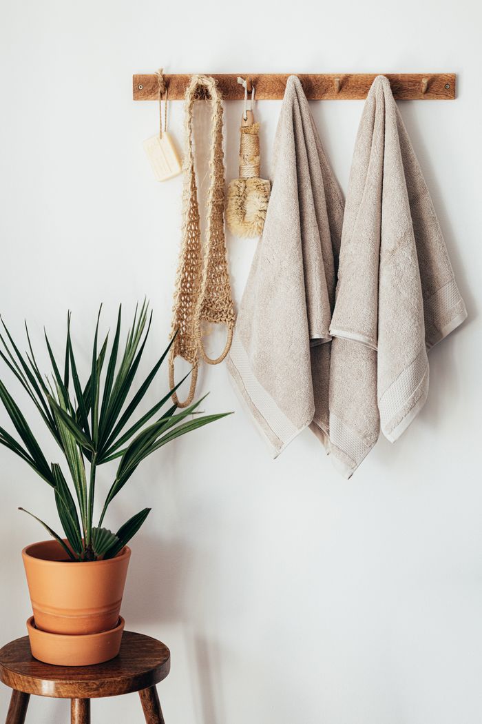 Stylish bathroom interior with houseplant on wooden table against white wall with hanging towels and set of eco friendly body care items